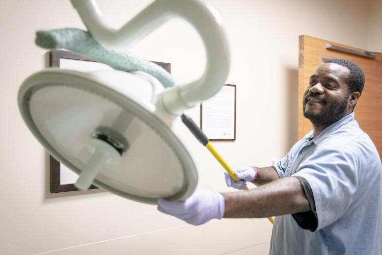 Derrick Christor dusts a lamp in an Emergency Department examination room.