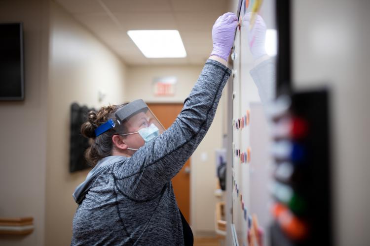 Dr. Katherine Buck, Director of Behavioral Medicine at JPS Health Network in Fort Worth, Texas, moves a magnet on a whiteboard to show she has taken her turn to see a patient in the Post COVID Recovery Clinic.